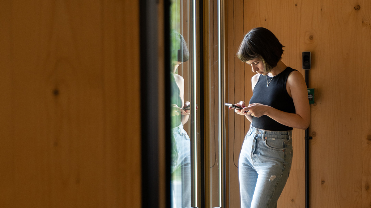 Eine Frau steht vor einer Glastüre und hält Smartphone in der Hand